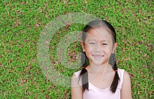 Smiling little Asian child girl with two ponytail hair lying on green grass in the garden