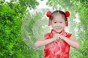 Smiling little asian girl in cheongsam respecting on traditional chinese new year festival against bamboo background