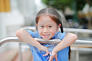Smiling little Asian girl in school uniform playful hanging at metal railing