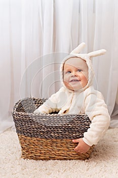 Smiling little baby boy in bunny easter costume sitting in the basket at home