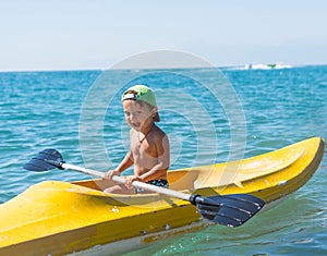 Smiling little baby boy in green baseball cap kayaking at tropical ocean sea in the day time. Positive human emotions, feelings, j