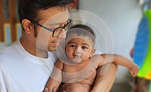 A smiling little baby boy held by his father with blurred background