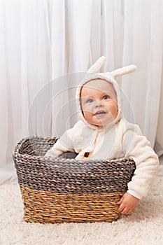 Smiling little baby in bunny easter costume sitting in the basket at home