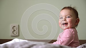 Smiling little baby girl with big eyes on bed looking at camera