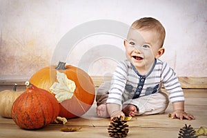 Smiling little baby sitting on the floor with pumpkins