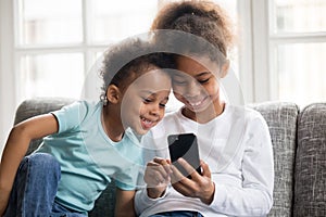Smiling little black kids play with smartphone together