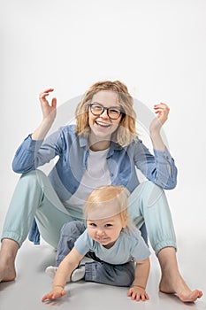 Smiling little blond blue-eyed girl daughter leaning on hands near young funny beautiful woman mother raising hands.