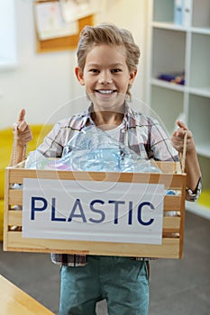 Smiling little boy in checkered shirt presenting box with plastic bottles