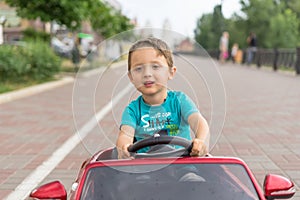 Smiling little boy driving by toy car. Active leisure and sports for kids. Portrait of happy little kid on the street. Funny cute
