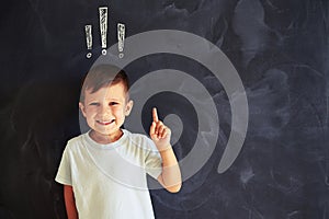 Smiling little boy with finger up against chalk drawing of exclamation marks