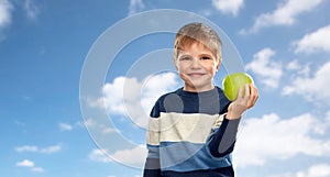 Smiling little boy with green apple over blue sky