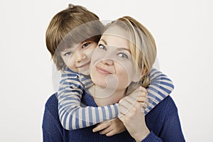 A smiling little boy and his mother hugging on the white background.