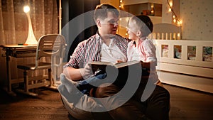 Smiling little boy listening to bedtime story his father is reading to him at night. Concept of child education and