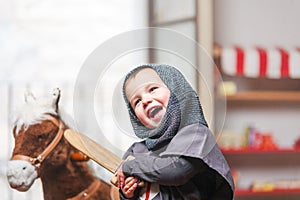 Smiling little boy plays knights with his wooden sword.