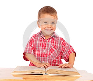 Smiling little boy reading book on the desk