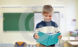 Smiling little boy reading book at school