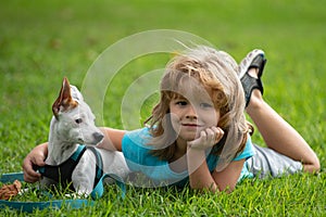 Smiling Little boy sitting on the grass with funny doggy. Happy child playing with dog on lawn.