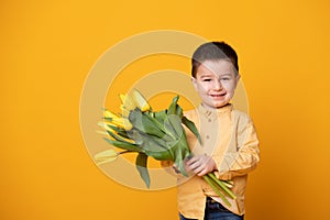 Smiling little boy on yellow studio background. Cheerful happy child with tulips flower bouquet