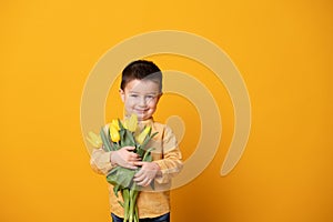 Smiling little boy on yellow studio background. Cheerful happy child with tulips flower bouquet