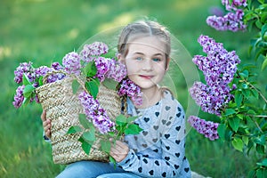 Smiling little cute blonde child girl 4-9 years with a bouquet of lilac in the hands in jeans and shirt