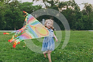 Smiling little cute child baby girl in denim dress walking, play with colorful kite and have fun in green park. Mother