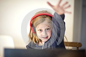 Smiling little European girl with headphones watching video lesson on computer