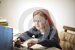 Smiling little European girl with headphones watching video lesson on computer