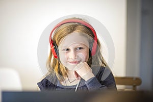 Smiling little European girl with headphones watching video lesson on computer