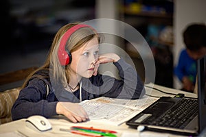 Smiling little European girl with headphones watching video lesson on computer