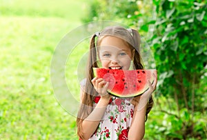 Smiling little girl with blue eyes eats a slice of watermelon