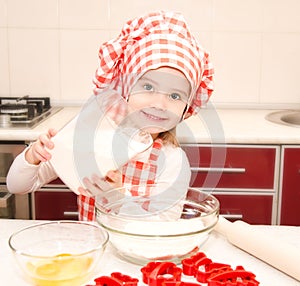 Smiling little girl with chef hat put flour for baking cookies