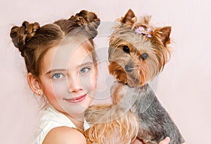 Smiling little girl child schoolgirl holding and playing with pet dog yorkshire terrier