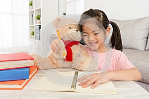 Smiling little girl doing homework with her teddy