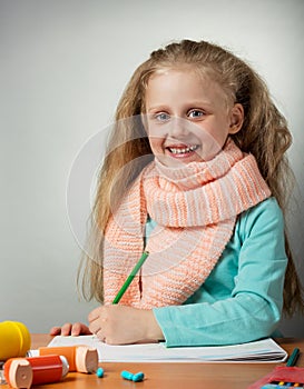 Smiling little girl draws at table, near inhaler on grey