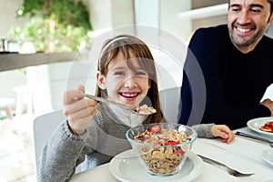 Smiling little girl eating cereals and smiling at the camera on kitchen at home