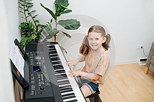 Smiling little girl enjoys playing electric piano at home. High angle.