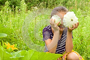 Smiling little girl having fun and harvesting fresh squashes in a garden. She is hiding her eyes behind two squashes
