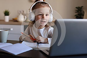 Smiling little girl in headphones handwrite study online using laptop at home photo