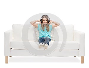 Smiling little girl in headphones sitting on sofa