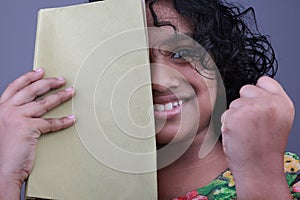 A smiling little girl with her face half covered by a book