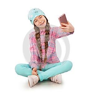 Smiling little girl holding mobile phone and making selfie on white background