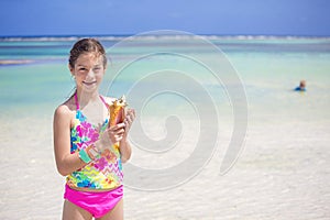 Smiling little girl holding a seashell on a scenic beach