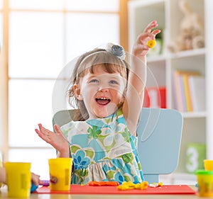 Smiling little girl is learning to use colorful play dough in a well lit room near window