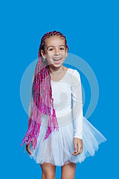 Smiling little girl with long pink hair, dressed in ballet white dress, on a blue background. Verical view.