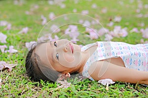 Smiling little girl lying on green grass with fall pink flower in the garden outdoor