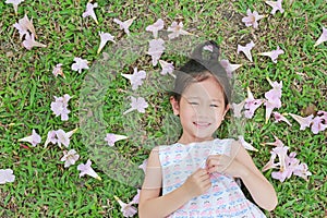 Smiling little girl lying on green grass with fall pink flower in the garden outdoor