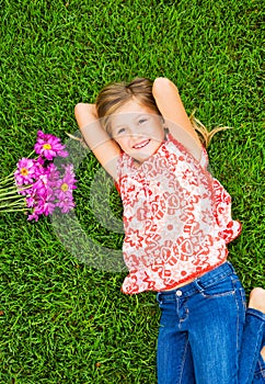 Smiling little girl lying on green grass with flowers