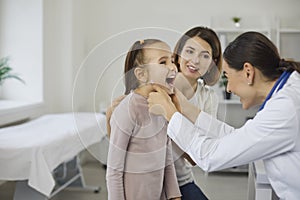 Smiling little girl opening mouth and showing throat for young woman doctor pediatrician