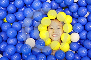 Smiling little girl playing with color plastic balls playground