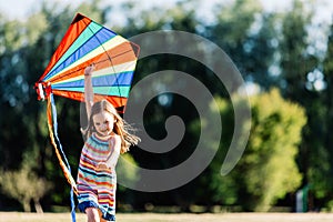 Smiling little girl playing with a colorful kite in the park.